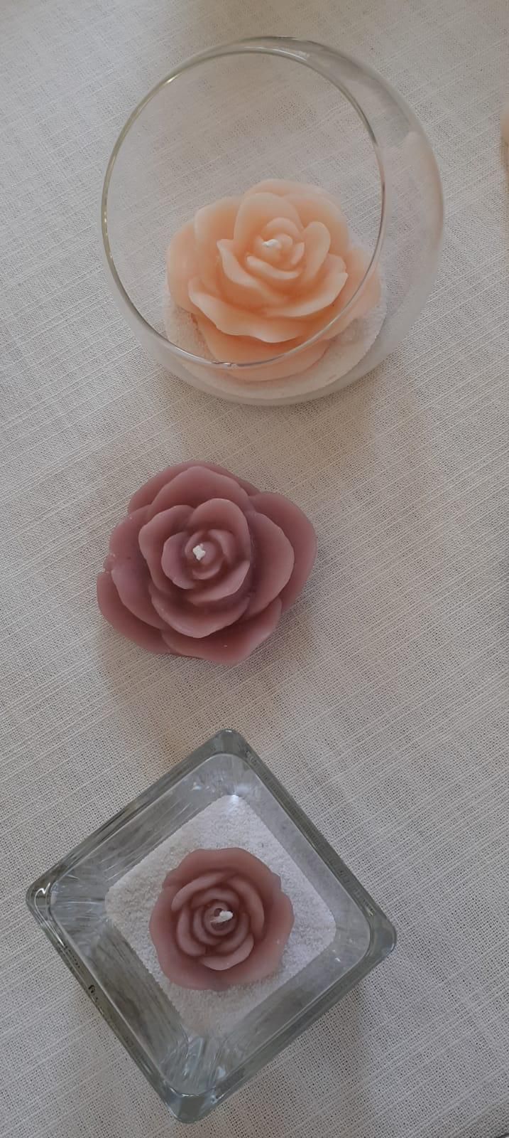 Tre candele a forma di rosa. Una in una ciotola di vetro, una sfusa e una in un piatto di vetro quadrato.