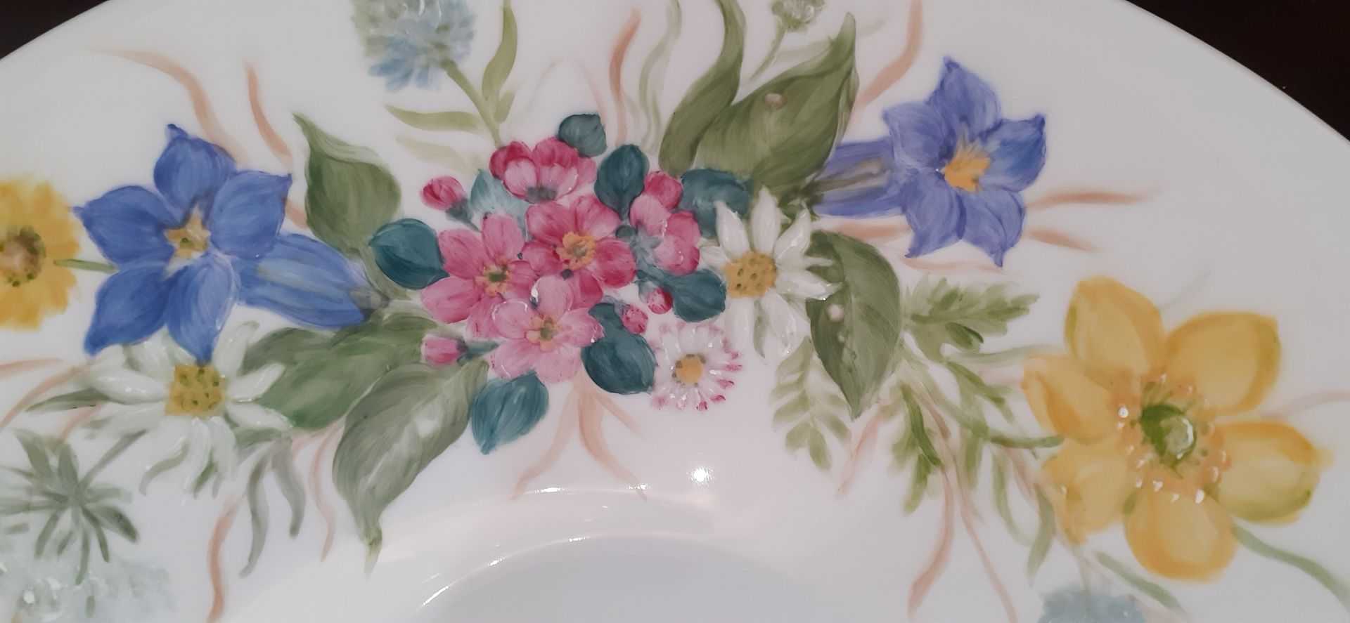Primo piano di un piatto bianco decorato con fiori acquerellati nelle tonalità del giallo, del blu e del rosa.