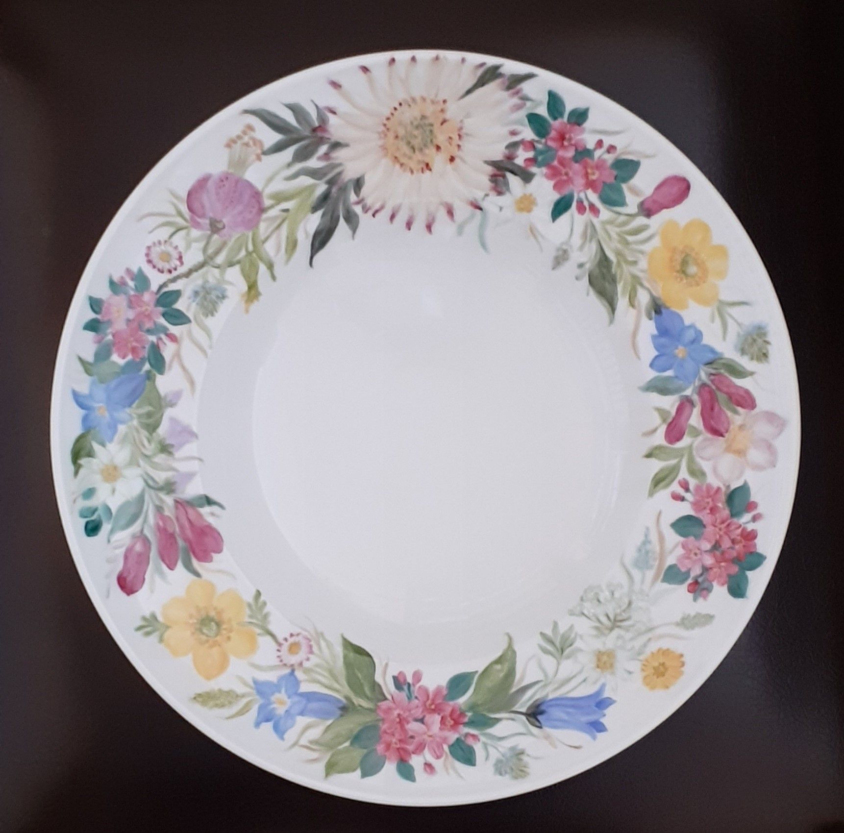 Piatto bianco con un disegno floreale ad acquerello lungo il bordo: fiori rosa, gialli, blu e verdi.