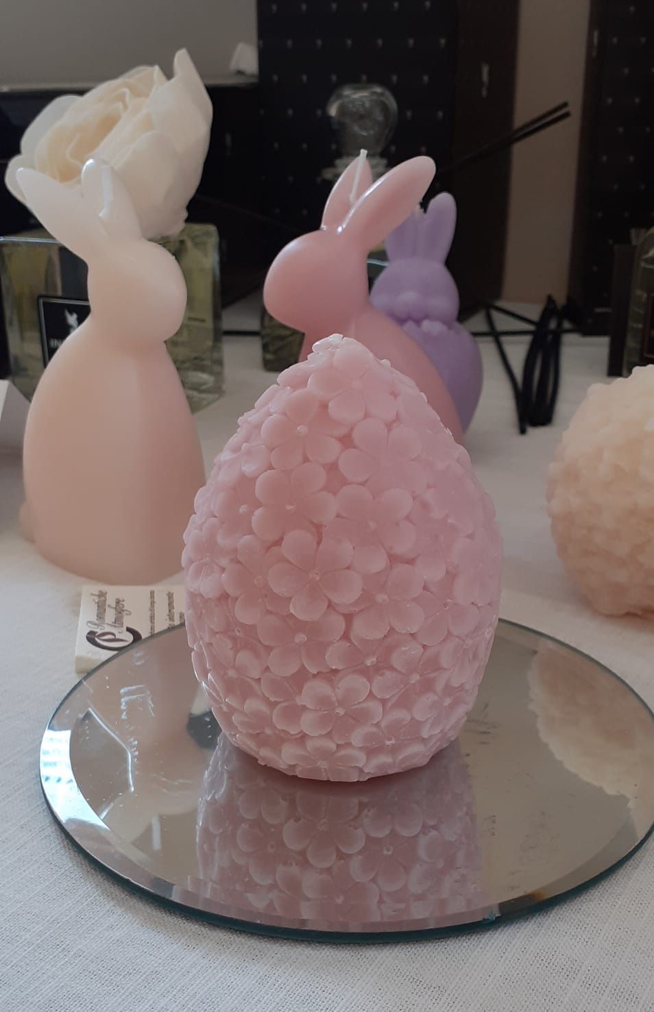 Una candela rosa a forma di uovo, circondata da altre candele color pastello