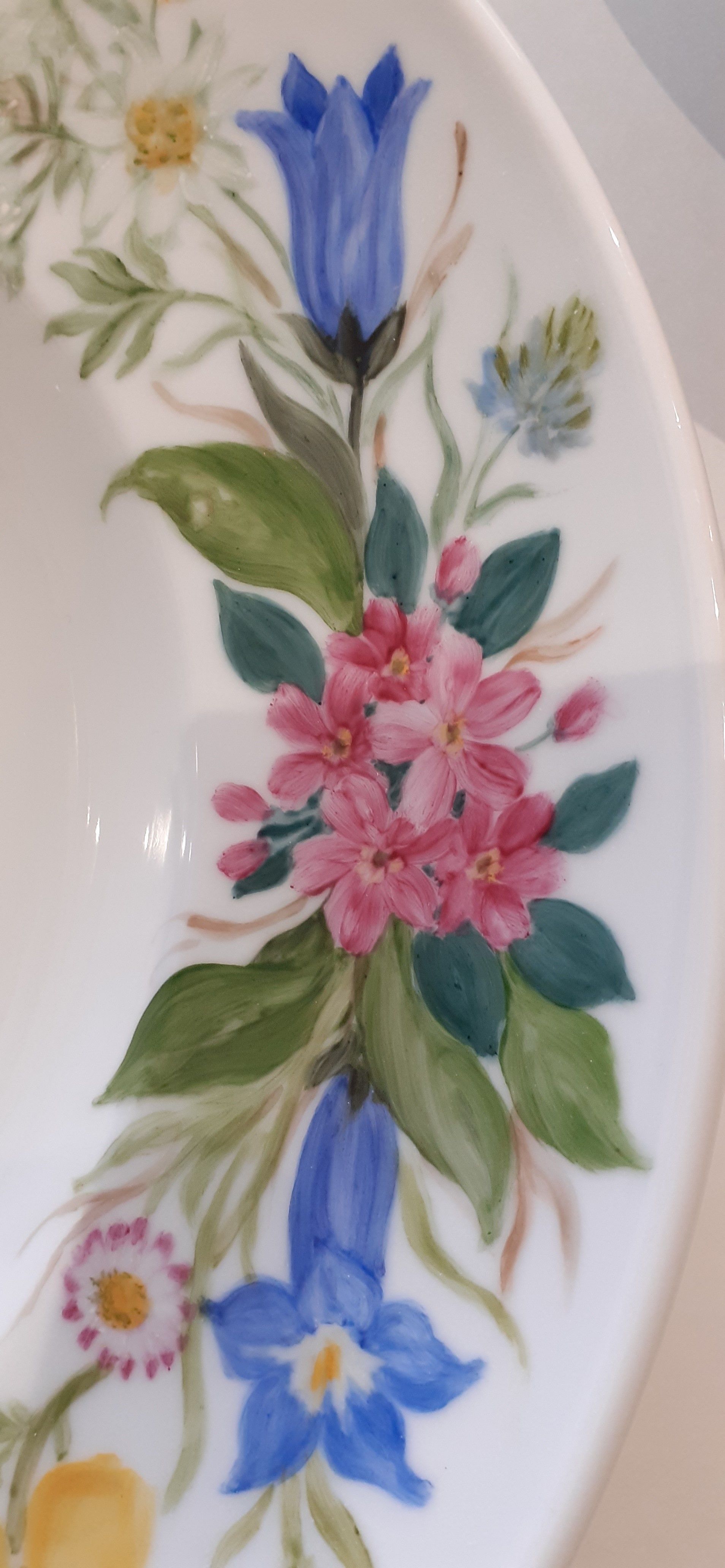 Disegno floreale su ceramica bianca, con fiori blu e rosa e foglie verdi.