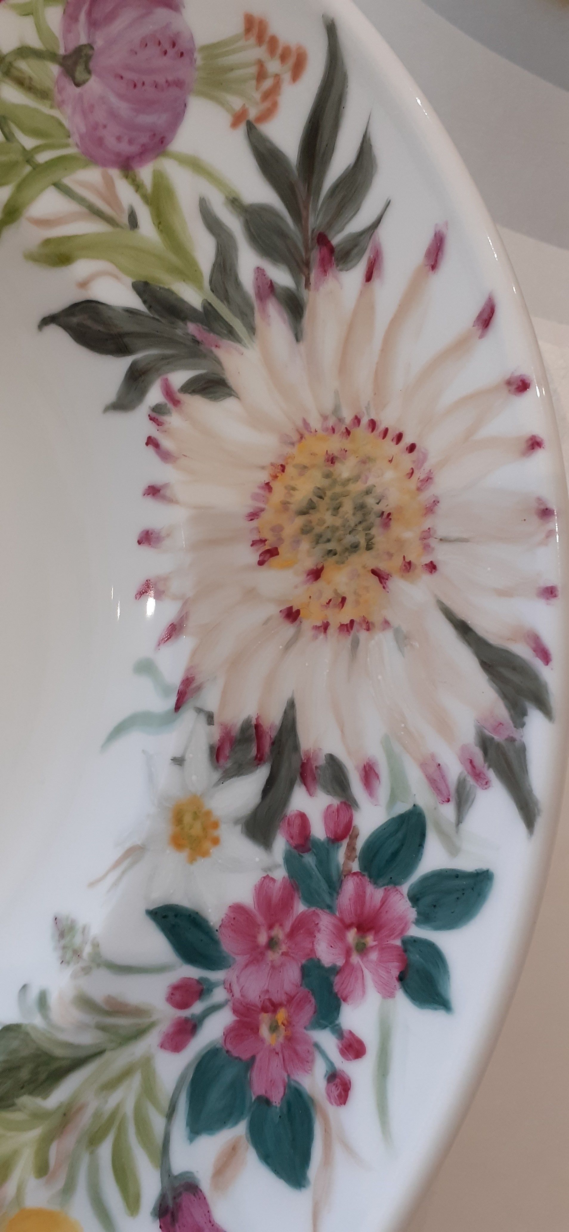 Piatto bianco con fiori dipinti a mano, tra cui una grande margherita bianca con punte rosa e piccoli fiori rosa.