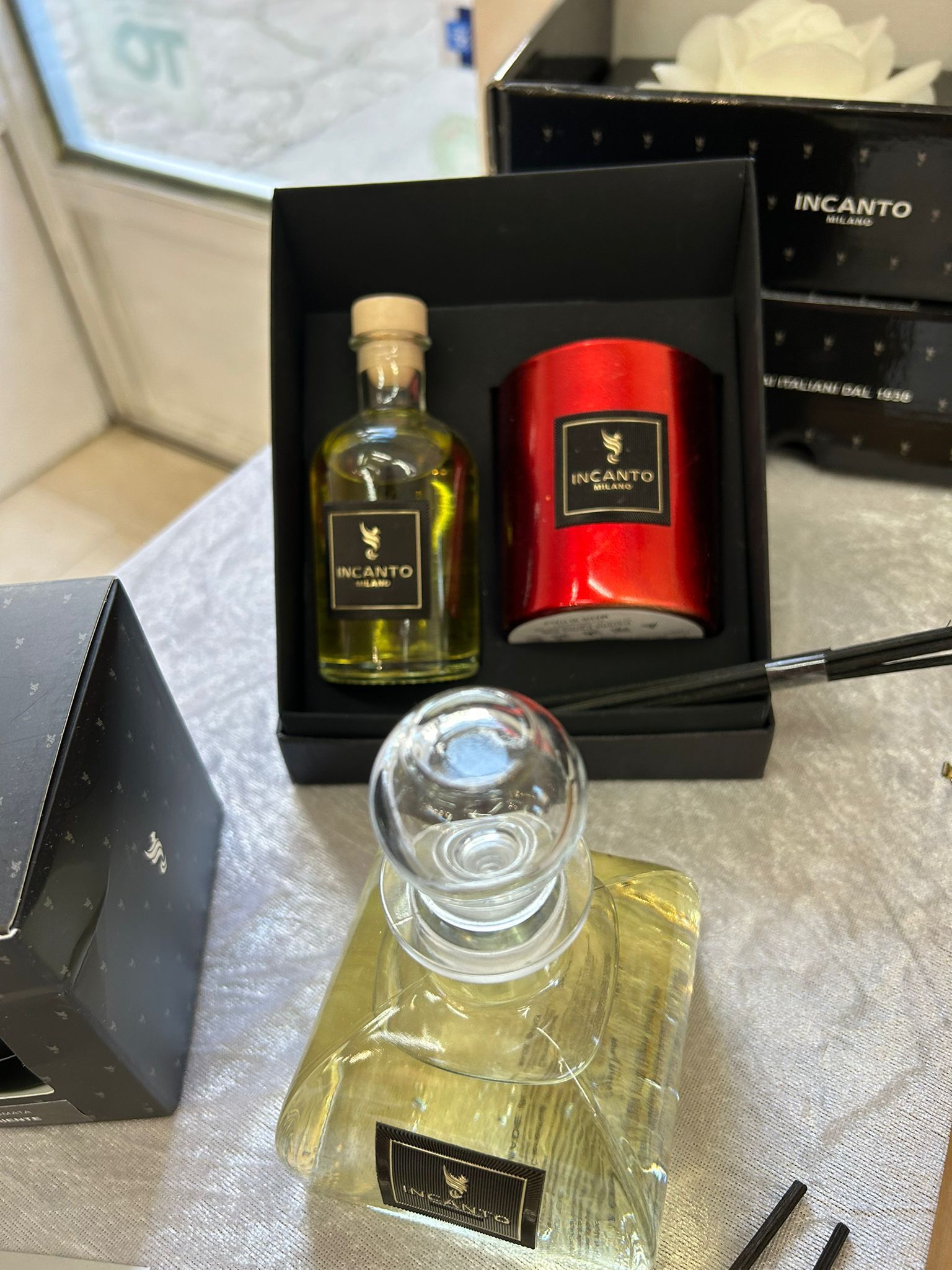 Set regalo con flacone di profumo, candela e diffusori; scatole nere, confezione dorata, superficie bianca.