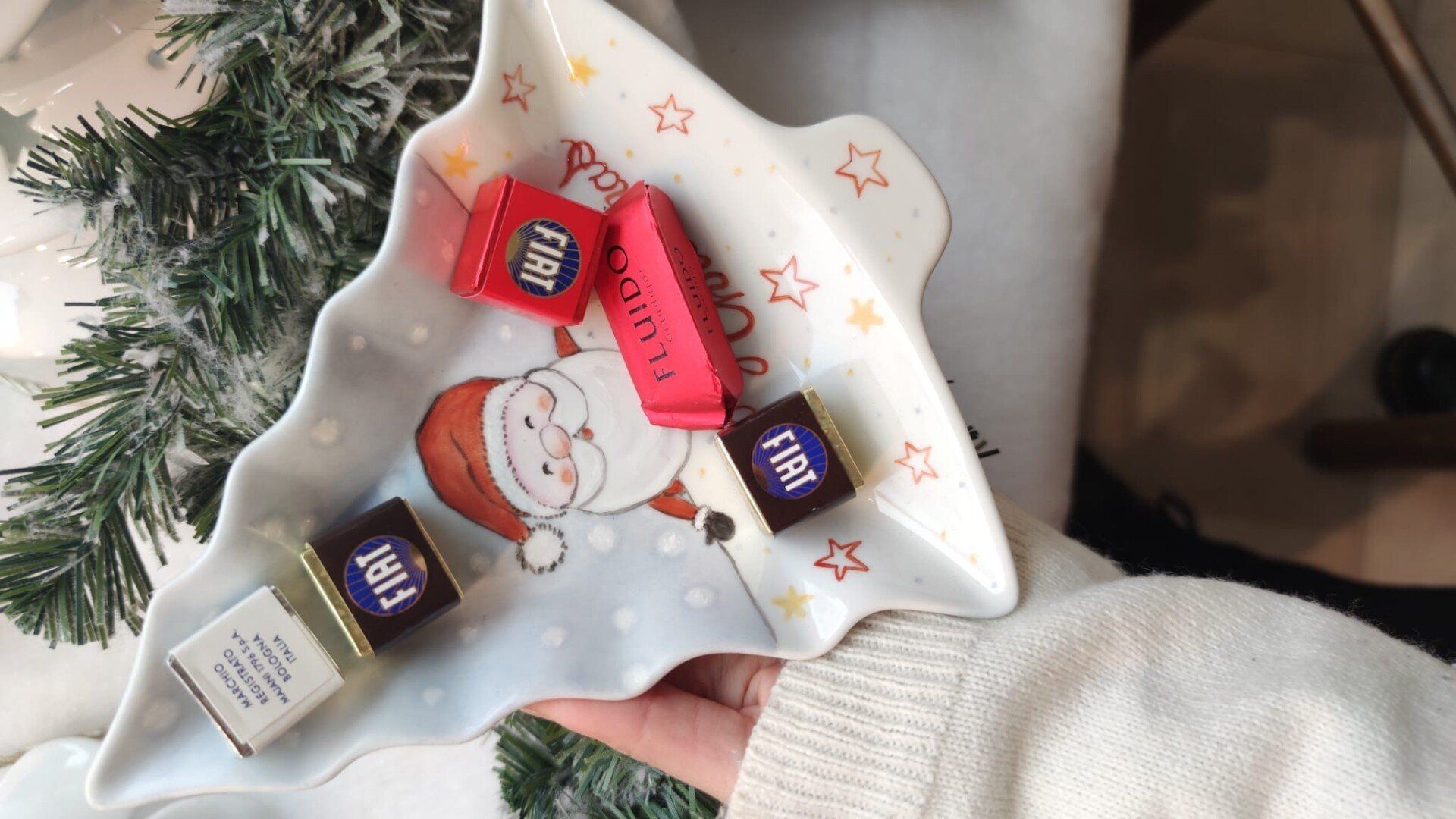 Mano che regge un piatto a forma di albero di Natale con cioccolatini; disegno di Babbo Natale e dettagli a forma di stella.