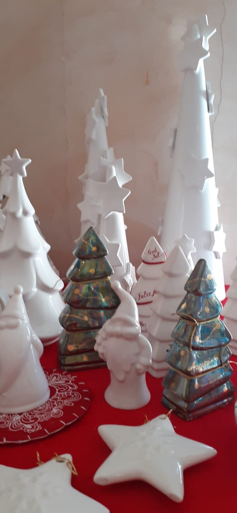 Decorazioni natalizie su una superficie rossa, tra cui alberi di Natale e stelle in ceramica bianca e verde.