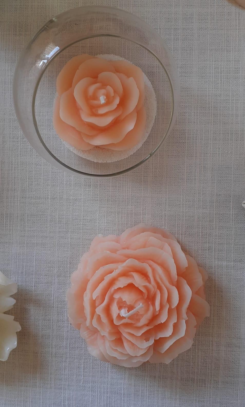Due candele color pesca a forma di fiore. Una galleggia in una ciotola di vetro