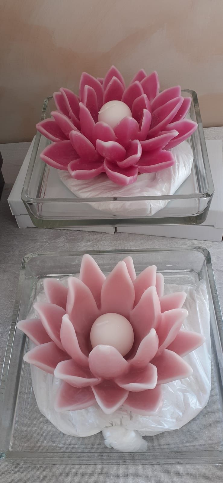 Due candele a forma di fiore di loto, una rosa e una rosa, sono posizionate in piatti di vetro su una superficie di legno.