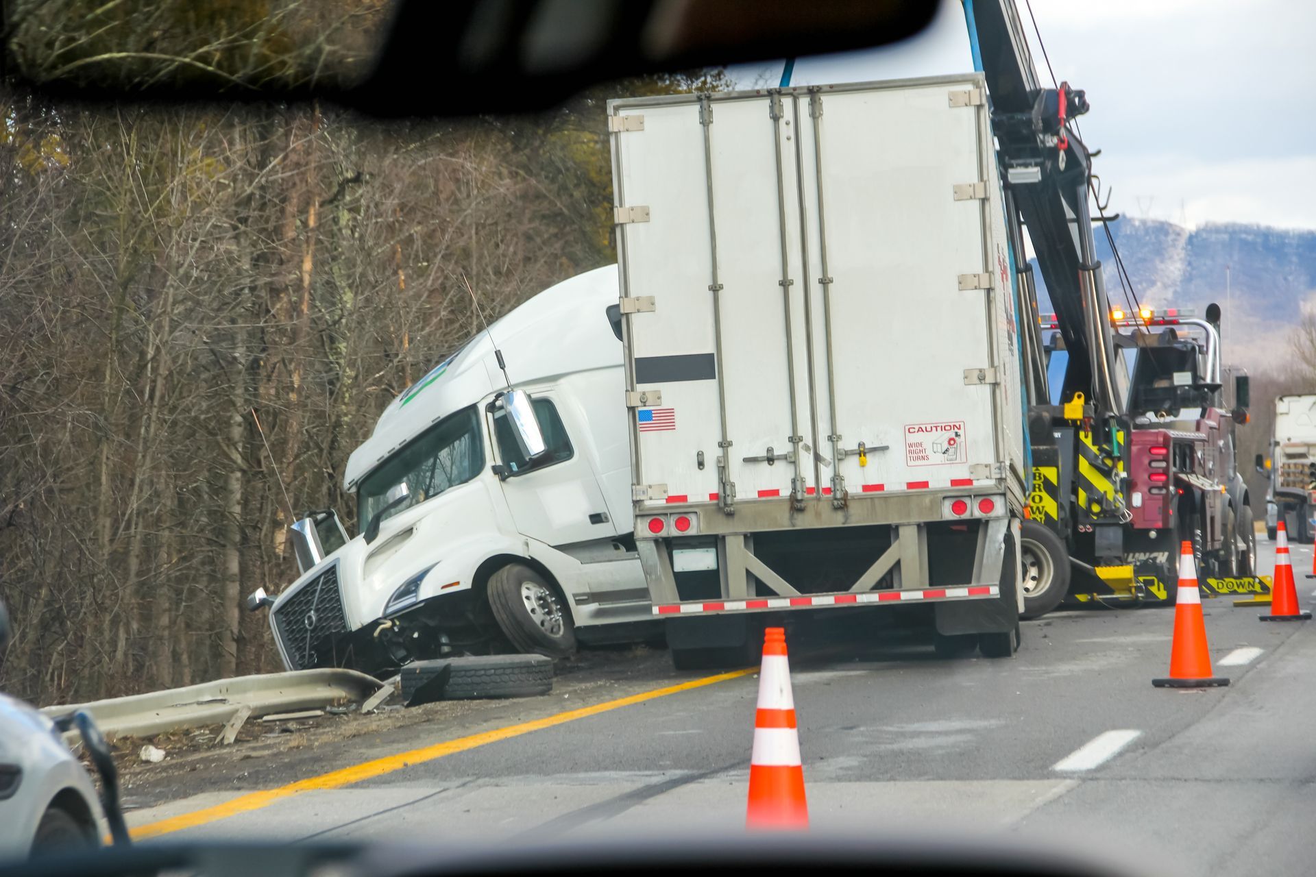 White semi-truck jackknifed on a wet road beside cones and a guardrail, blocking traffic