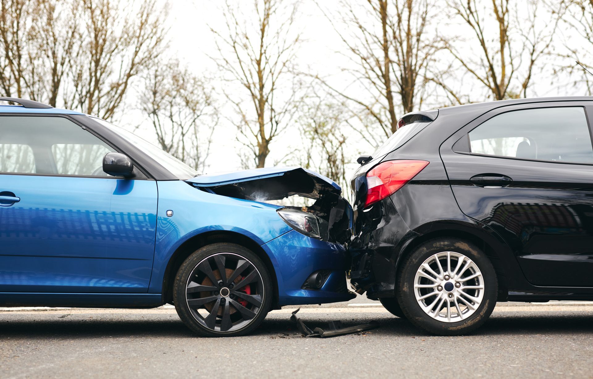 Blue and black cars with heavy front-end collision on a road, likely a rear-end crash