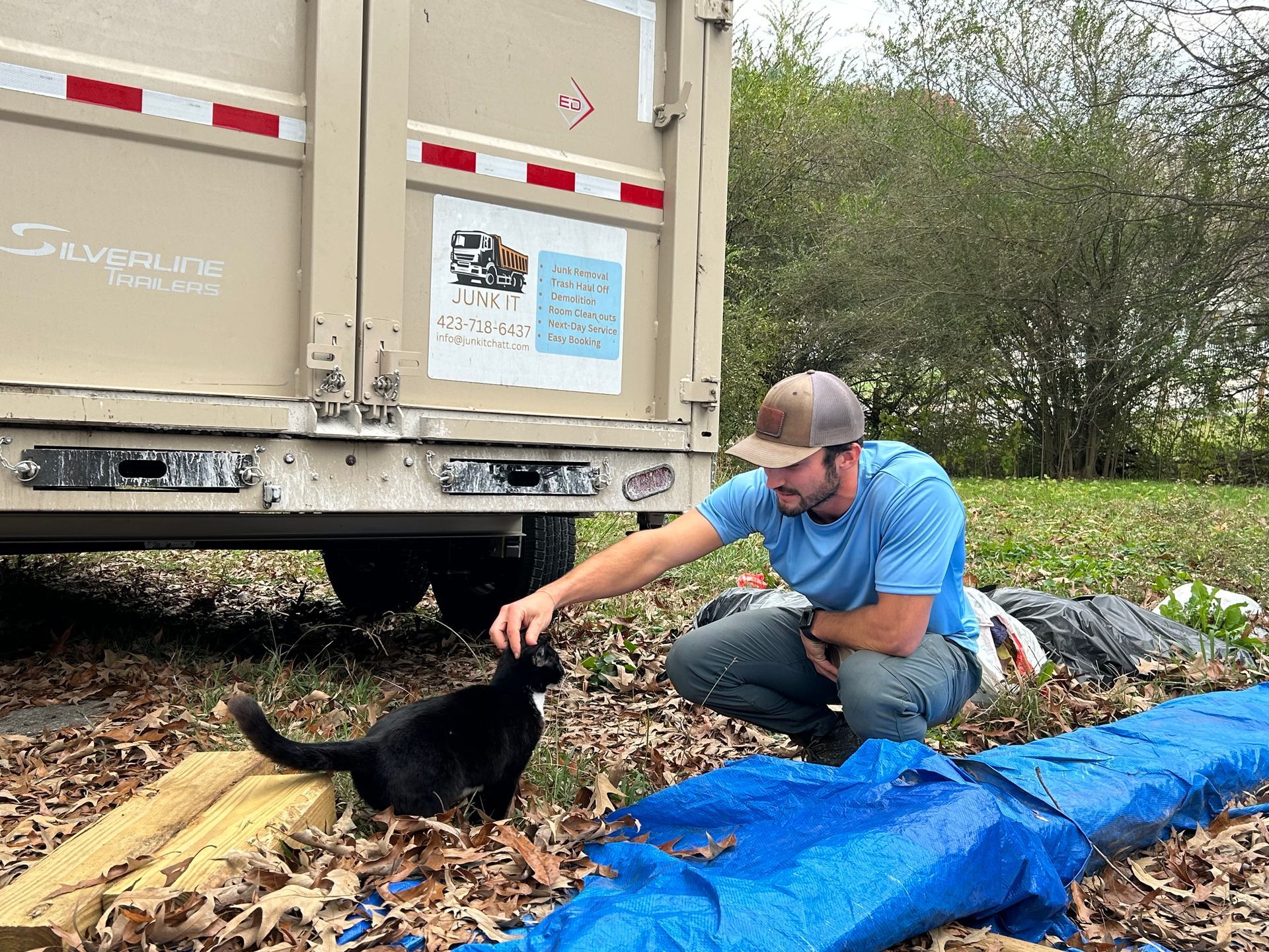 A man is petting a black cat in front of a truck.
