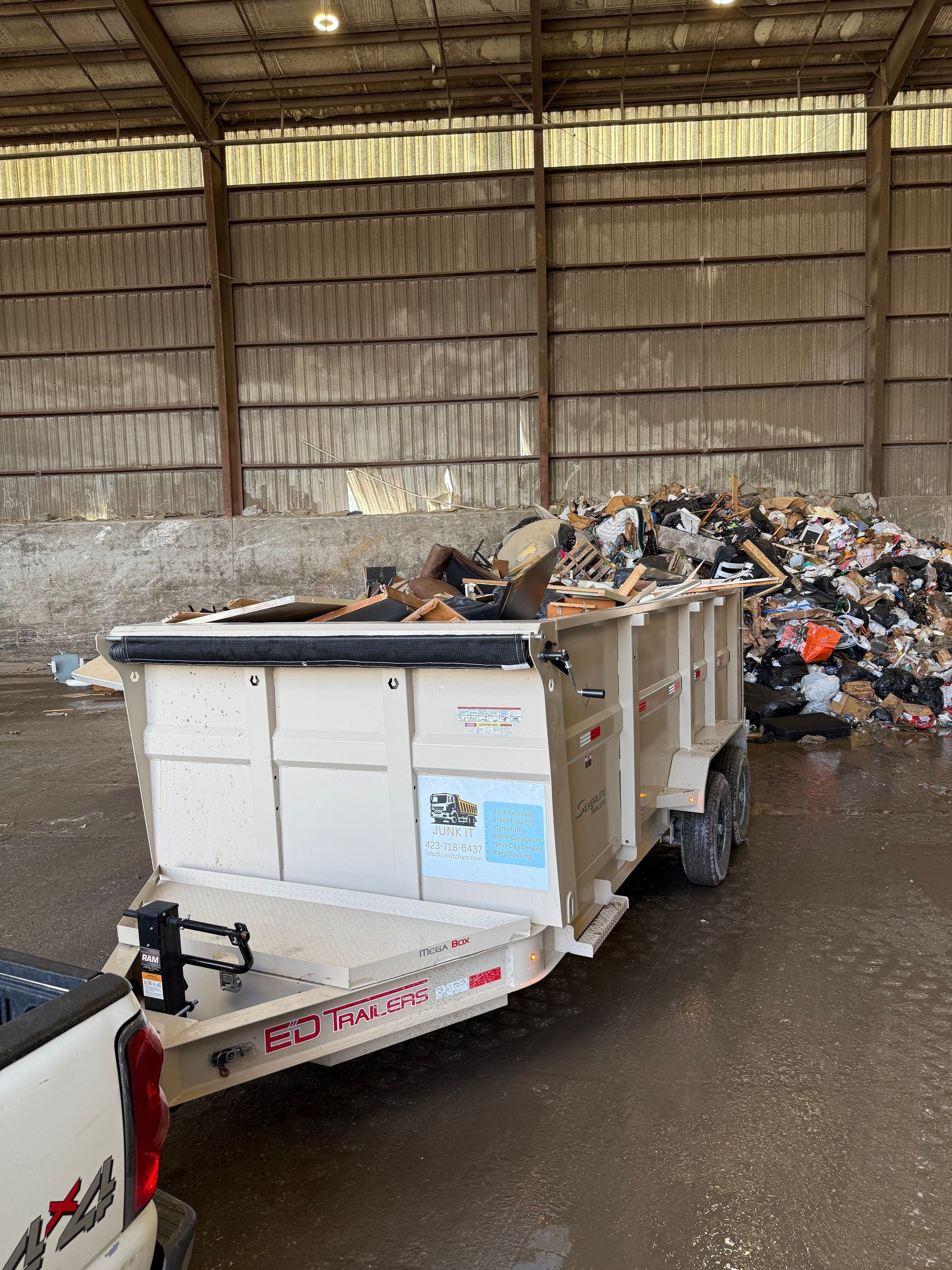 A trailer is being pulled by a truck in a warehouse filled with trash.