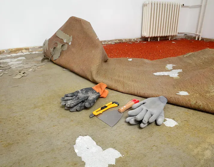 A piece of carpet is laying on the floor next to a pair of gloves and a spatula.