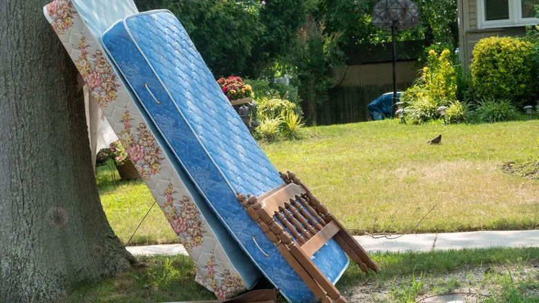 Two mattresses are stacked on top of each other on the side of the road.