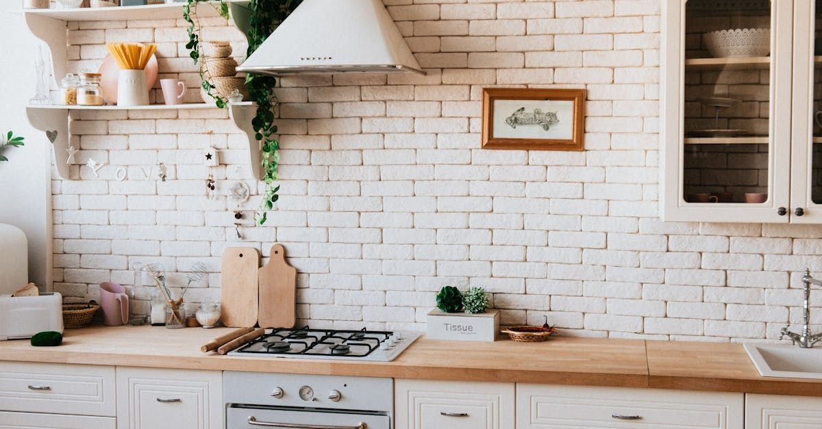 A kitchen with white cabinets , a stove , a sink and a brick wall.