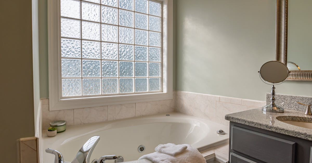 A bathroom with a jacuzzi tub , sink , mirror and window.