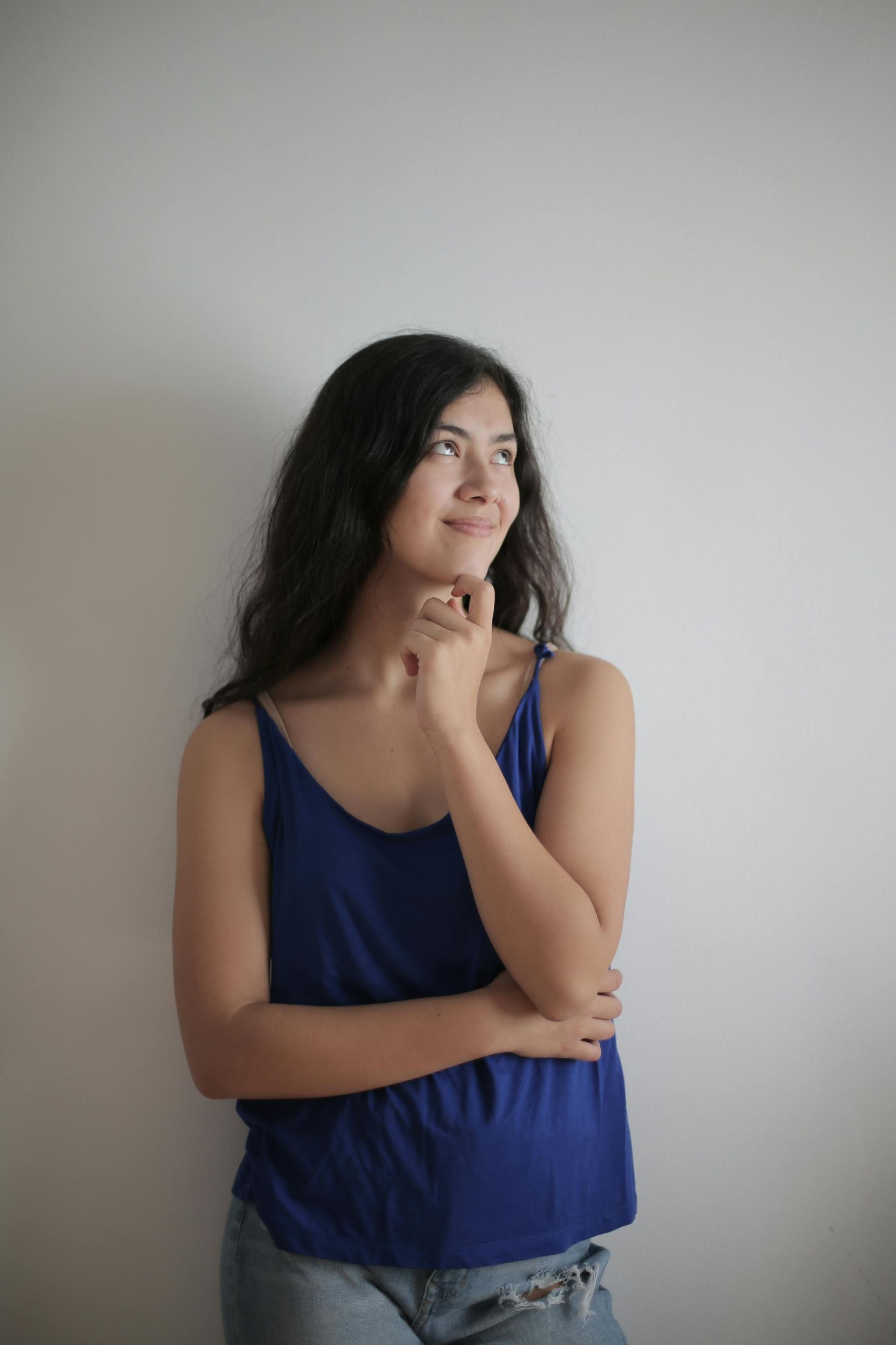 A woman in a blue tank top is standing in front of a white wall.