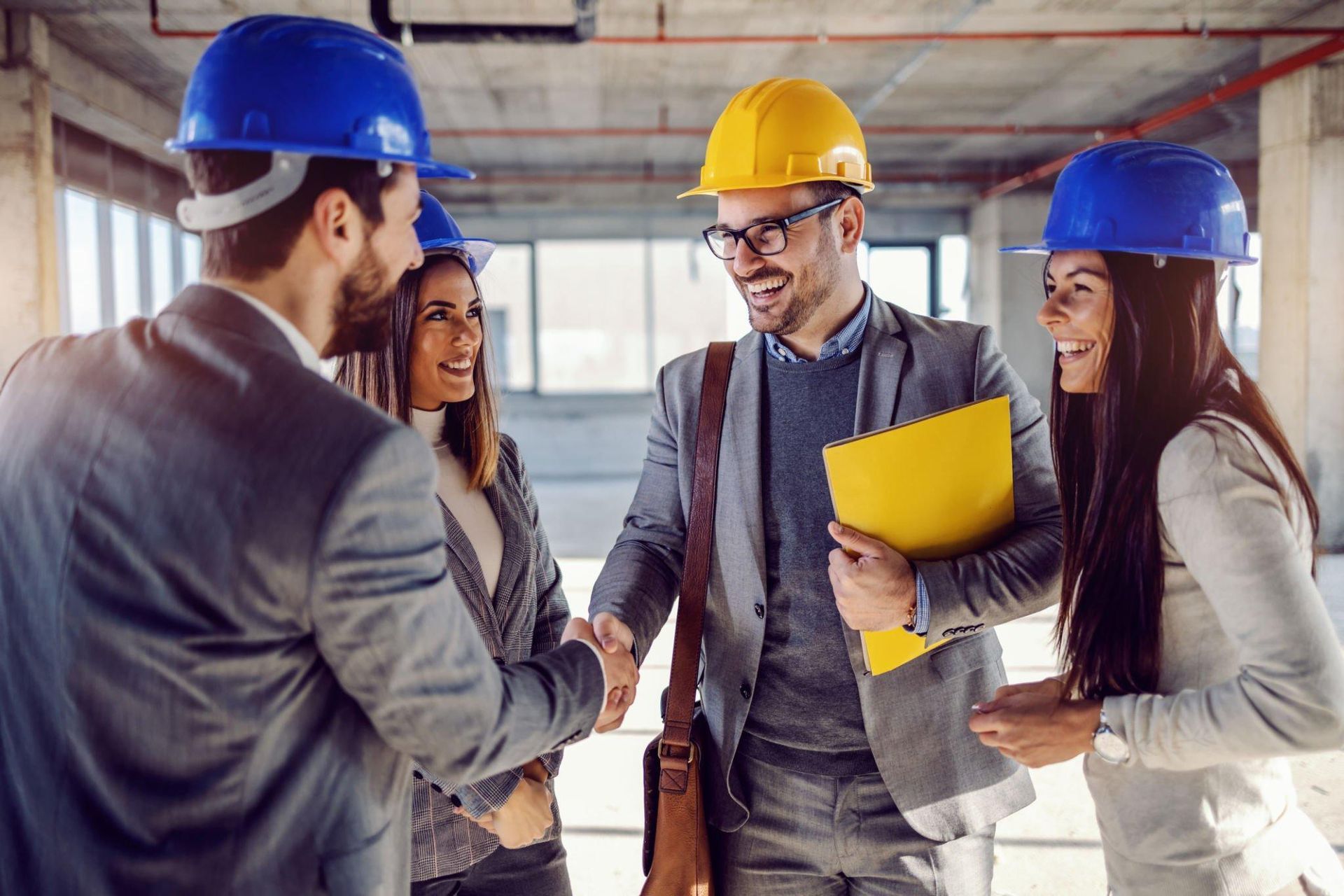 A group of people wearing hard hats are shaking hands in a building under construction.