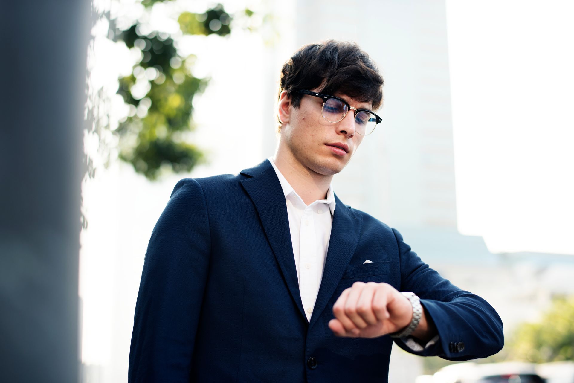 A man in a suit and glasses is looking at his watch.