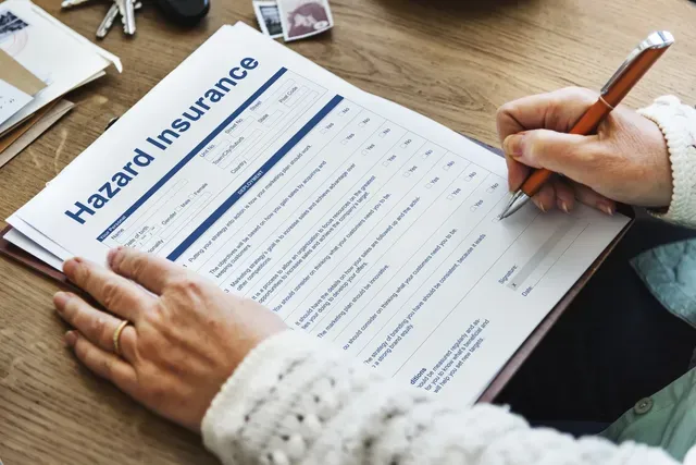 A person is filling out a hazard insurance form with a pen.