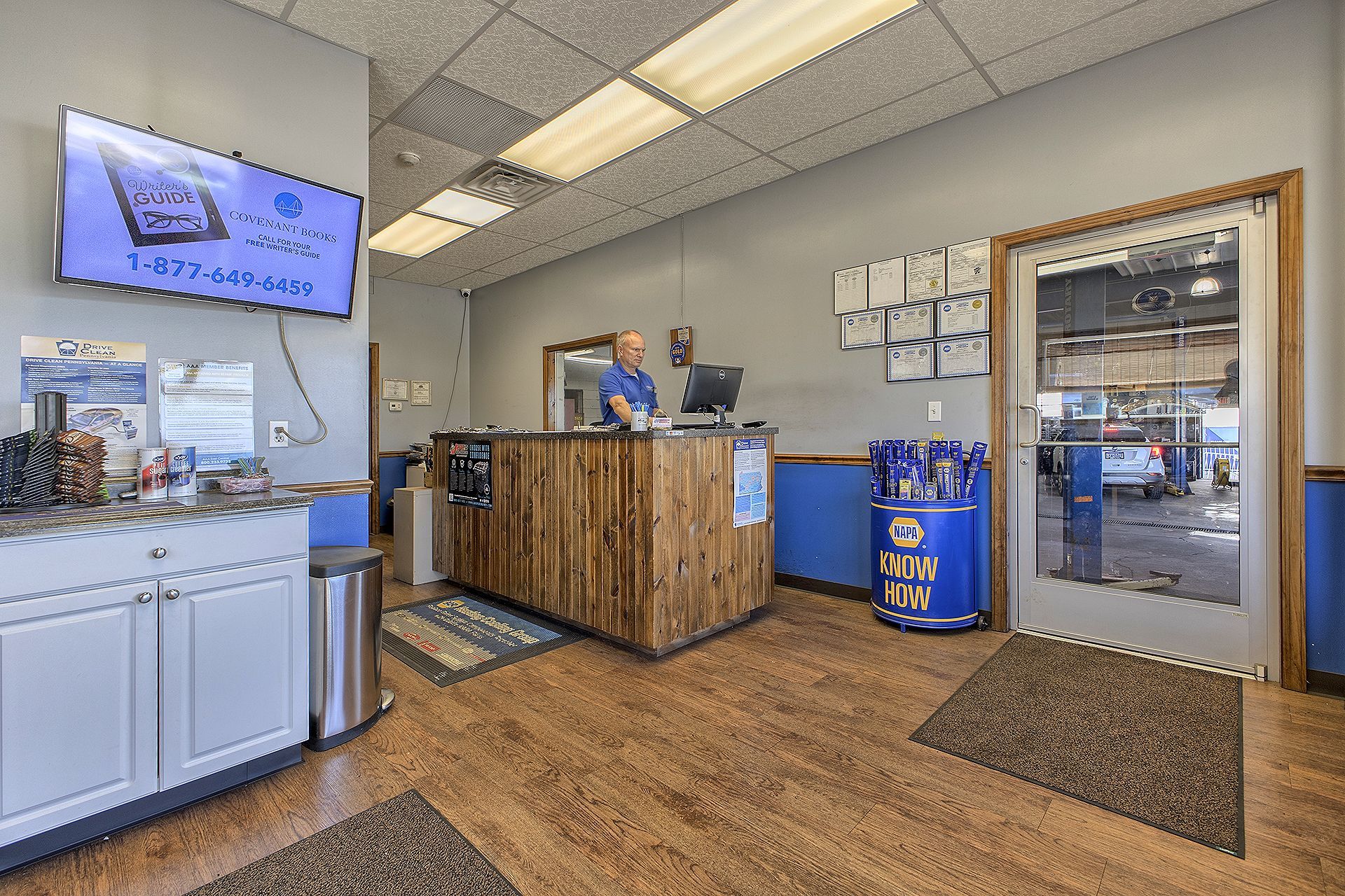 A front desk area in an auto repair shop with a receptionist, a service counter, and a view into the garage. | Allwine Curry Inc