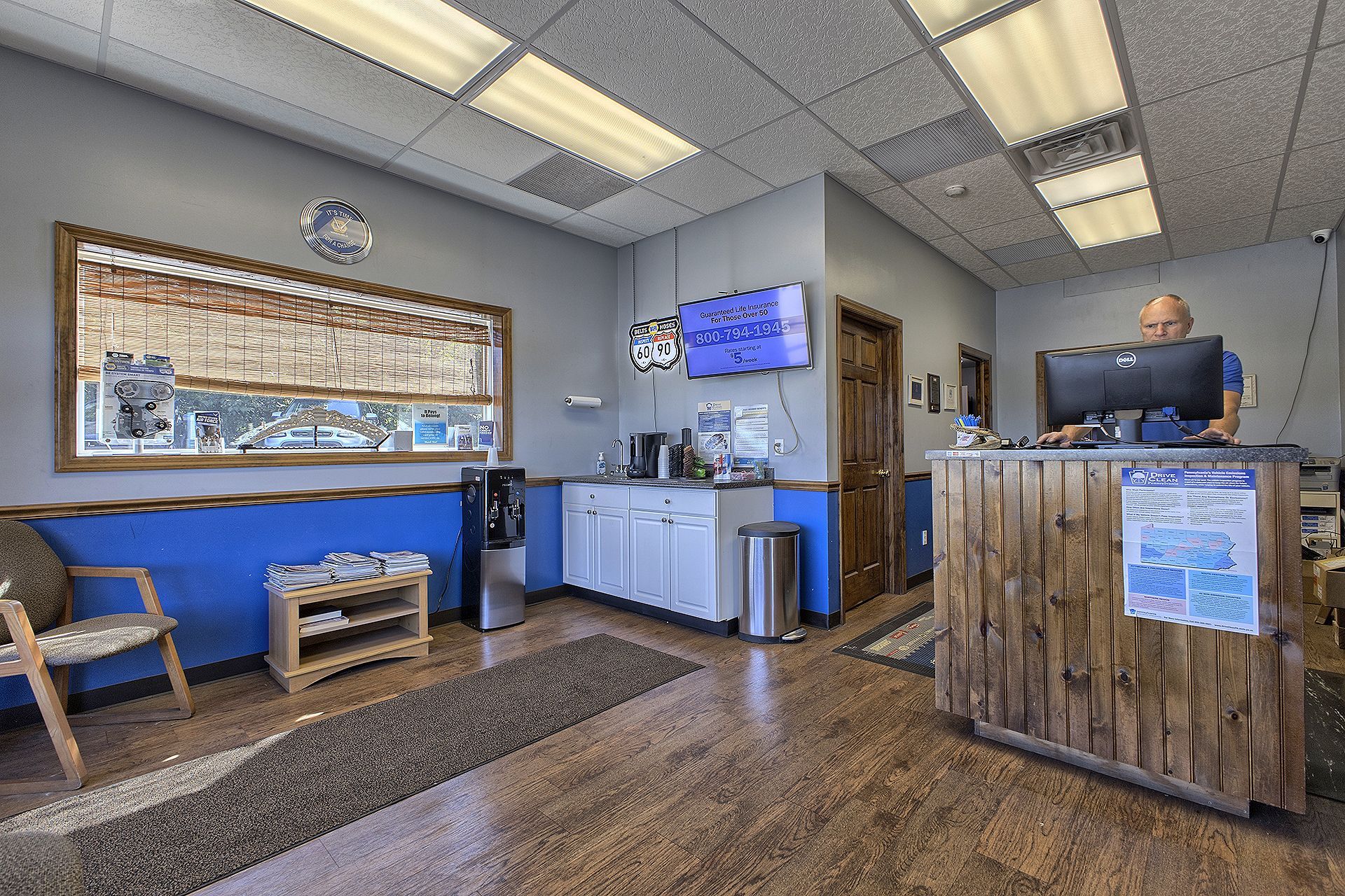 A reception area with a wood-paneled desk, a person working at a computer, blue walls, a window, and seating. | Allwine Curry Inc