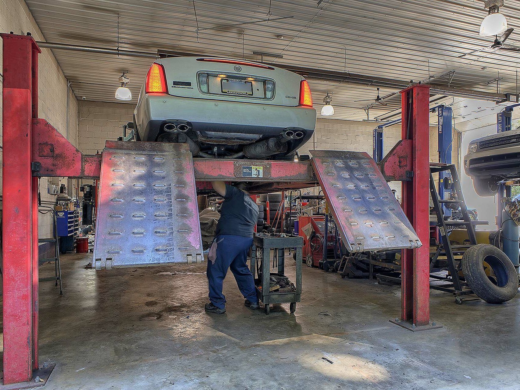 A mechanic works under a car elevated on a hydraulic lift inside an automotive repair shop. | Allwine Curry Inc