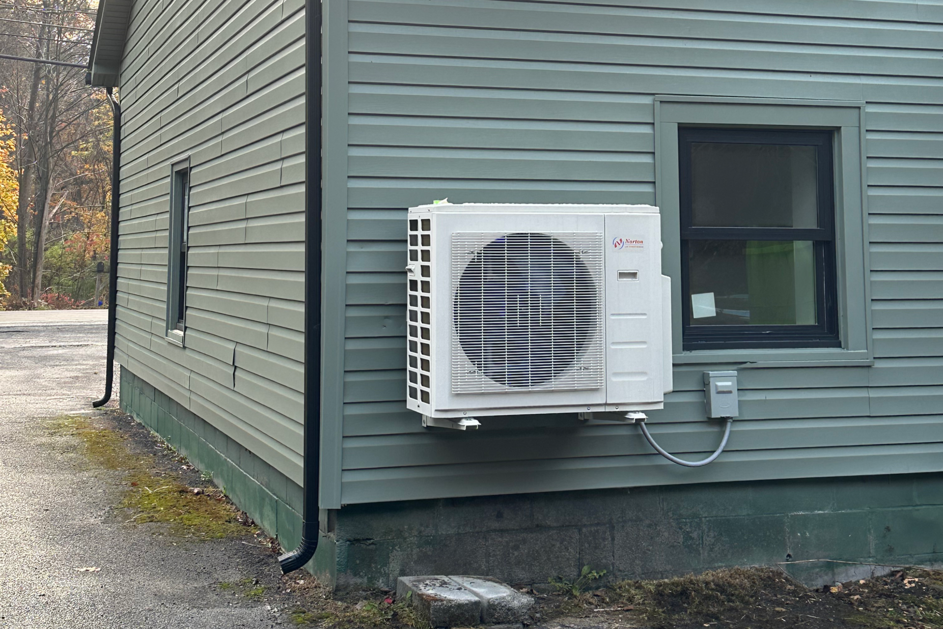 An outdoor air conditioning unit under a wooden deck next to a brick wall.
