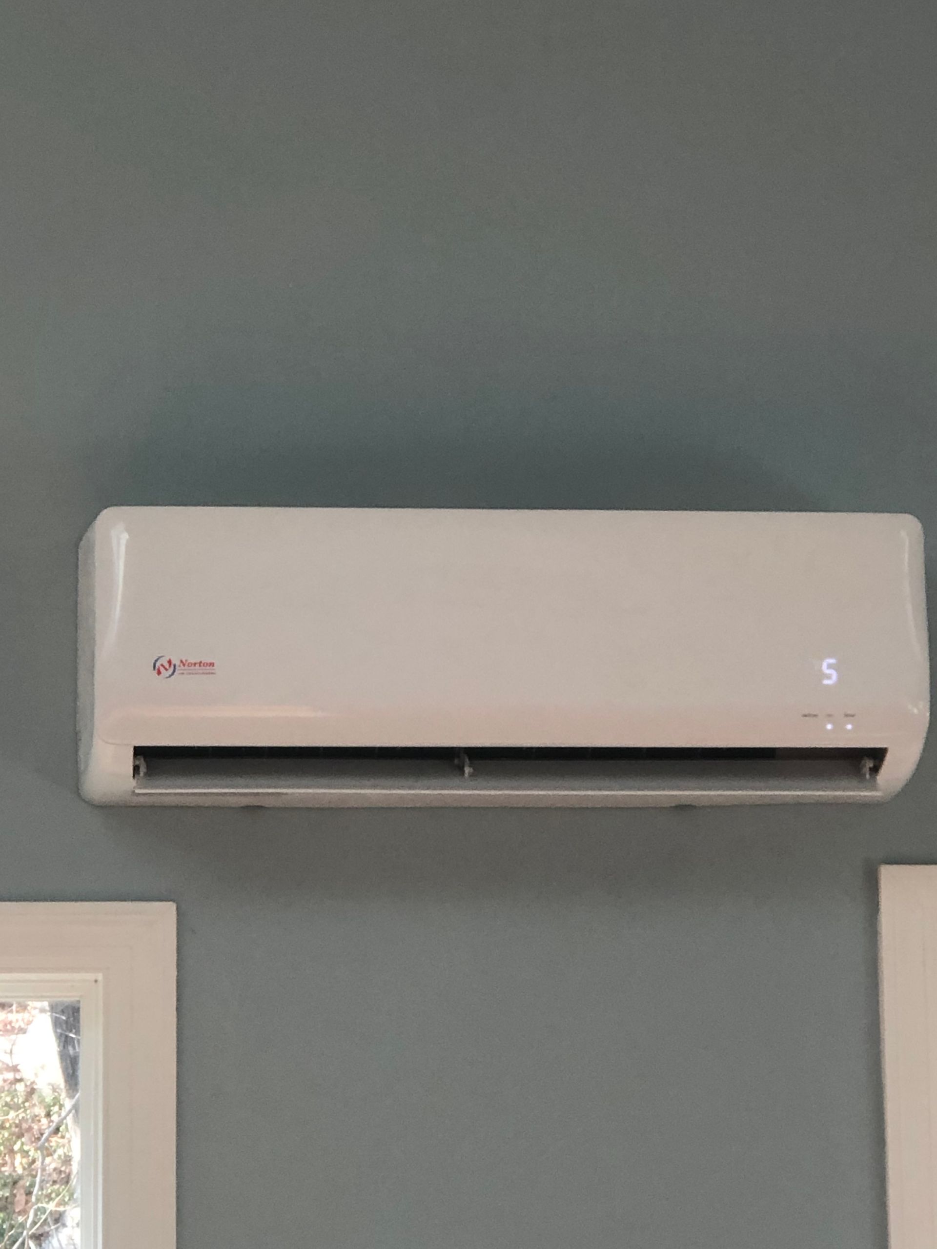 Air conditioner on a wall in a bedroom with two beds. White, grey, and light blue decor.
