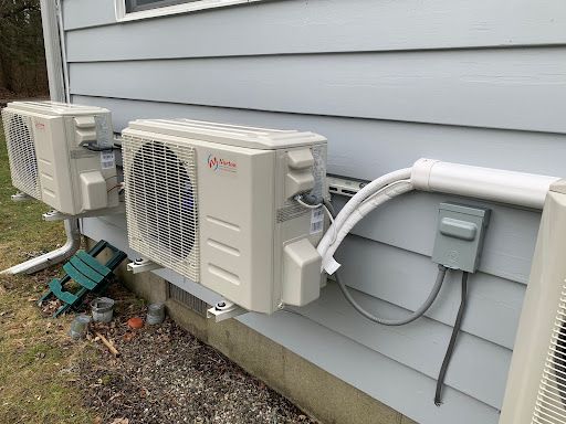 Several beige air conditioning units mounted on a light blue house exterior. White conduit pipes connect them.