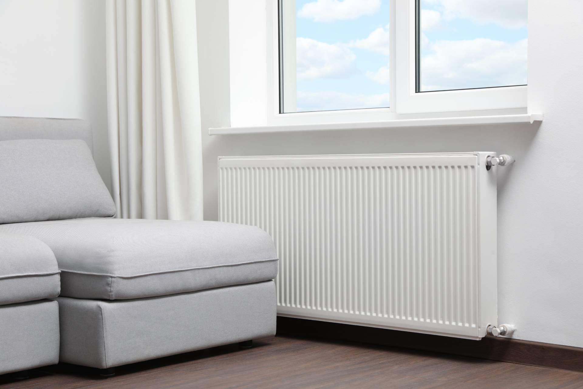 Gray sofa and radiator by a window with a view of the sky.