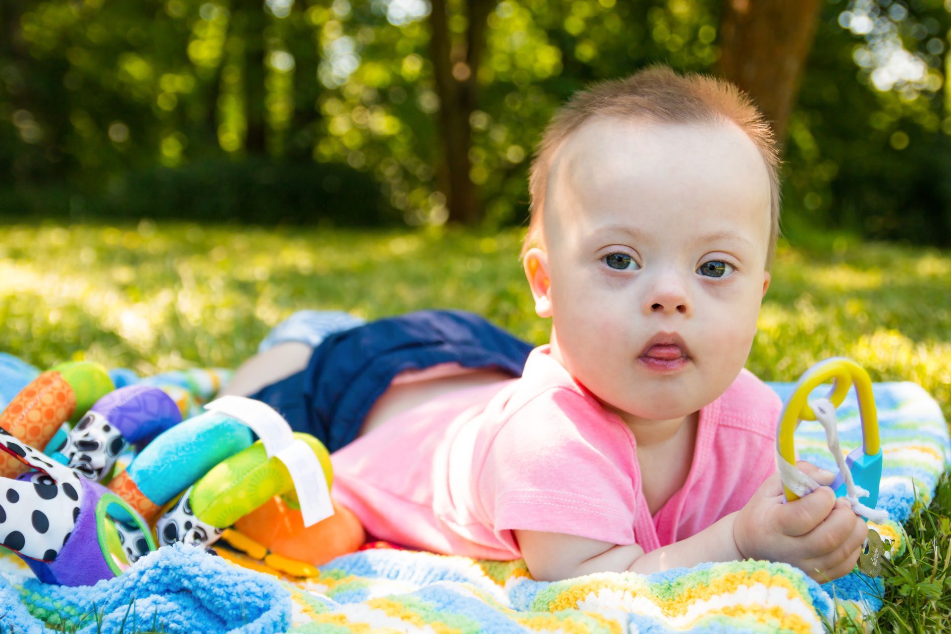 A young baby laying on a blanket outside, with toys.