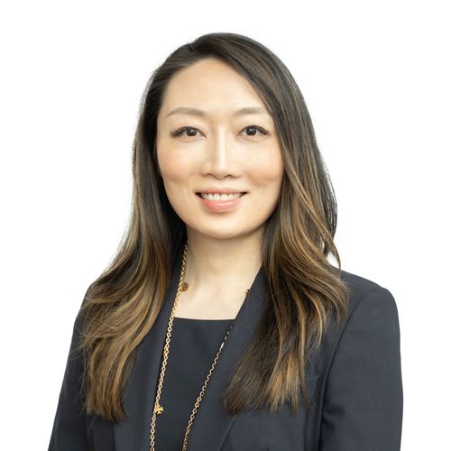 Asian woman with long hair, in a dark suit, smiling.