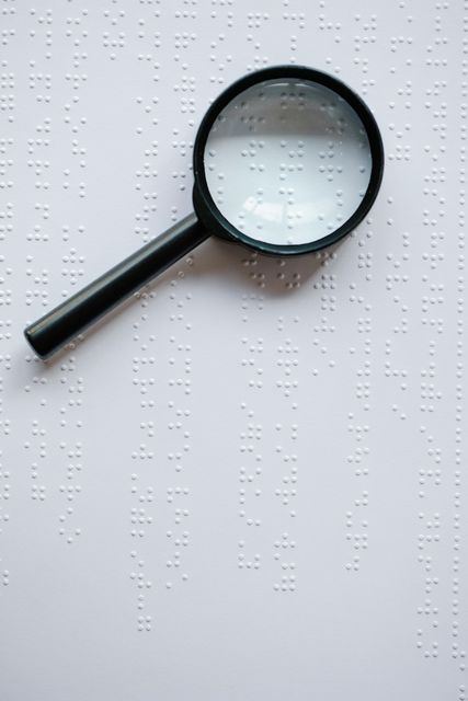 Magnifying glass over Braille text, examining dots on a white surface.