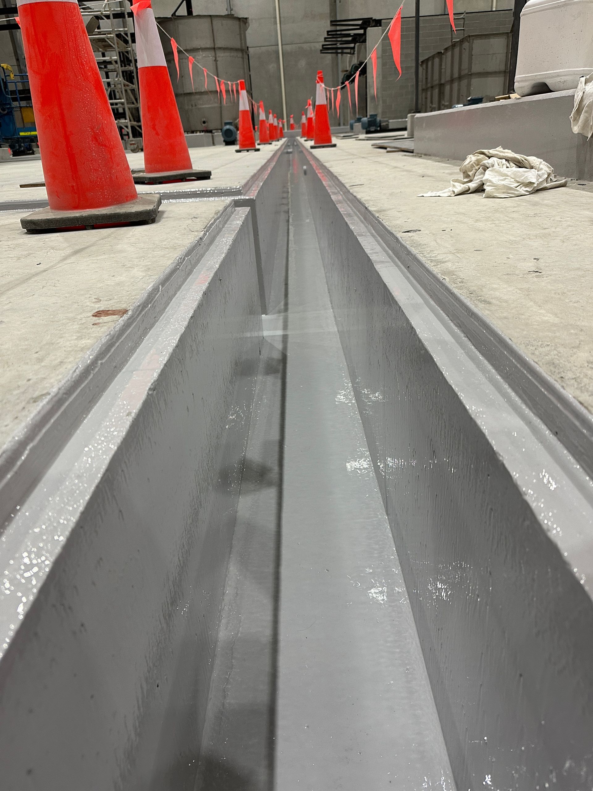 Concrete drainage channel with gray interior, lined with orange safety cones in a construction area.