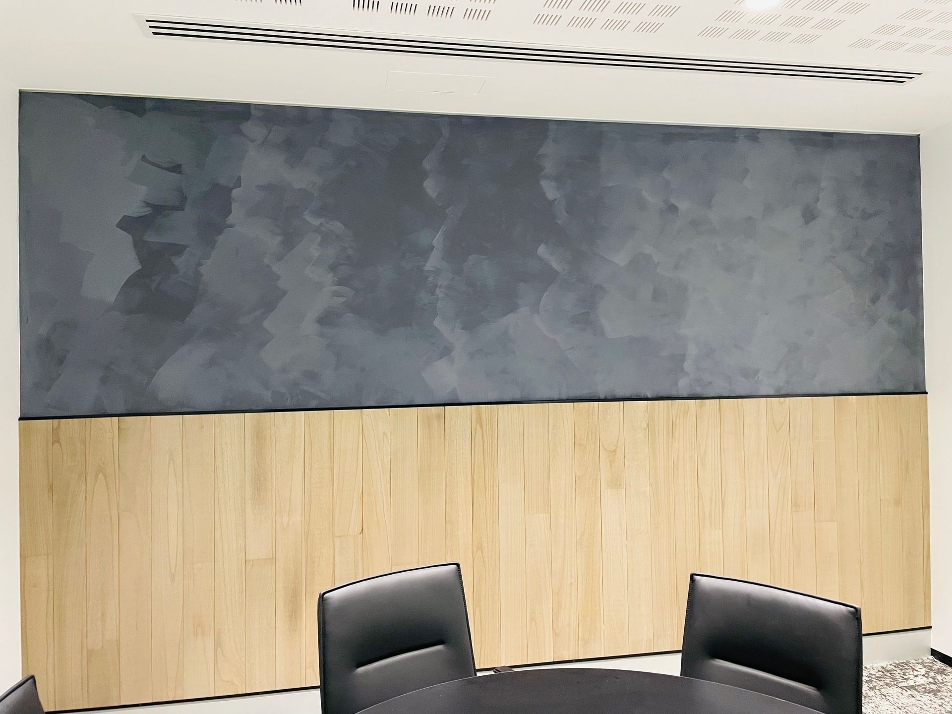 Conference room with gray painted upper wall and wooden paneling below; black chairs around a table.