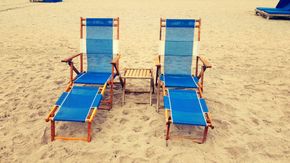 Two blue striped beach chairs on sand with a small table between them