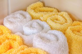 Plush white and yellow towels rolled in a neat stack on a shelf