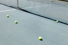 Four yellow tennis balls scattered on a blue court near the net.