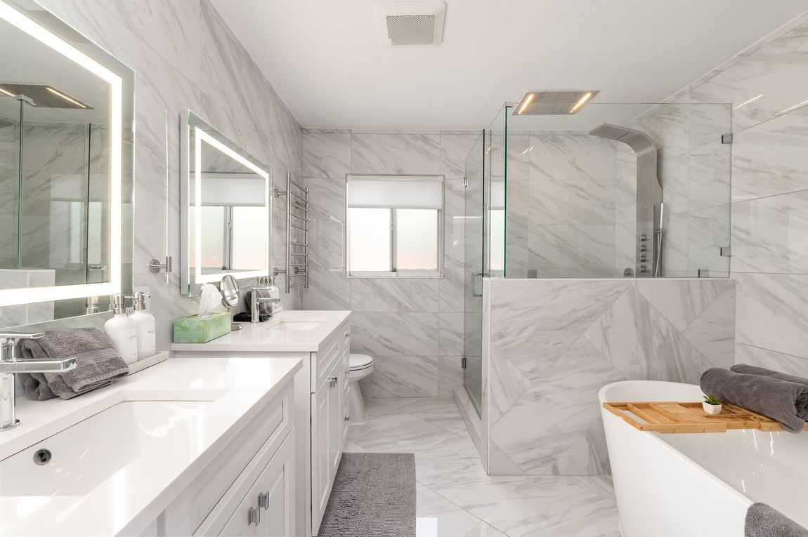 Bright marble bathroom with double vanity, large mirror, and freestanding tub by a glass shower.