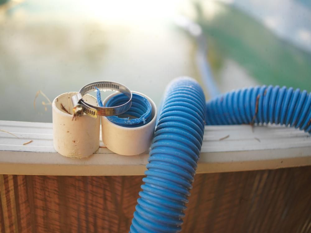 A Blue Hose is Sitting on Top of a Wooden Fence Next to a Swimming Pool — Gold Coast Leak Detection in Mudgeeraba, QLD