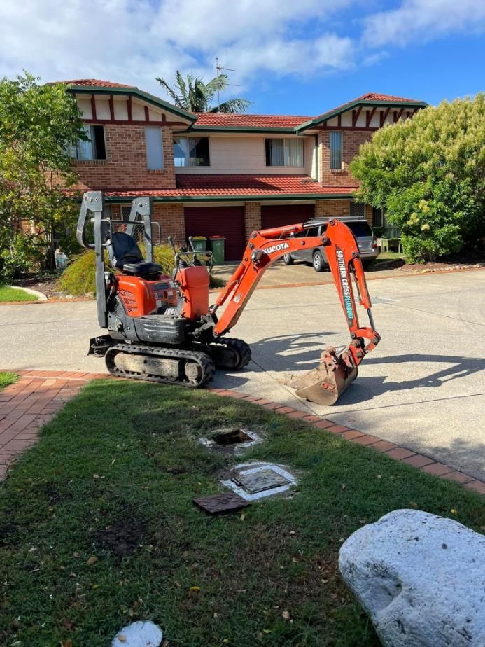 A Small Red Excavator is Parked in Front of a House — Gold Coast Leak Detection in Mudgeeraba, QLD