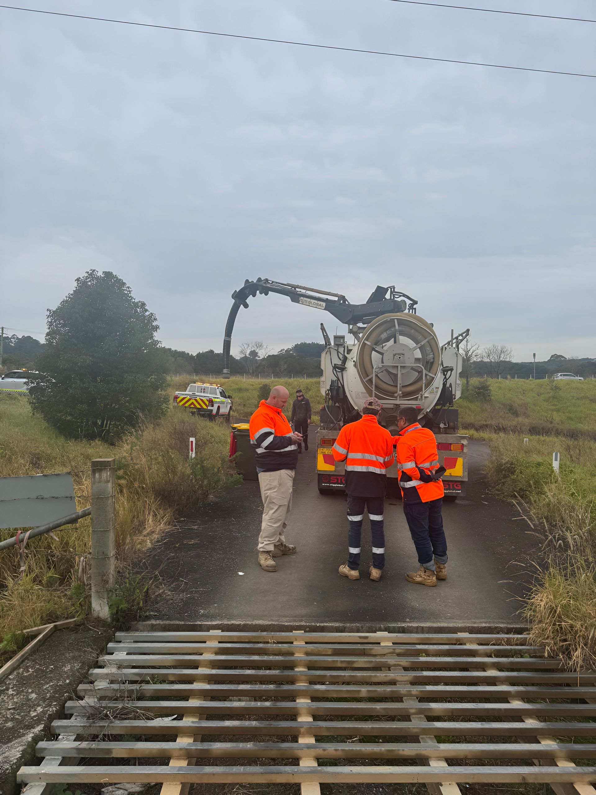 Workers in Orange Vests Stand Near a Truck Dispensing Material — Gold Coast Leak Detection in Mudgeeraba, QLD