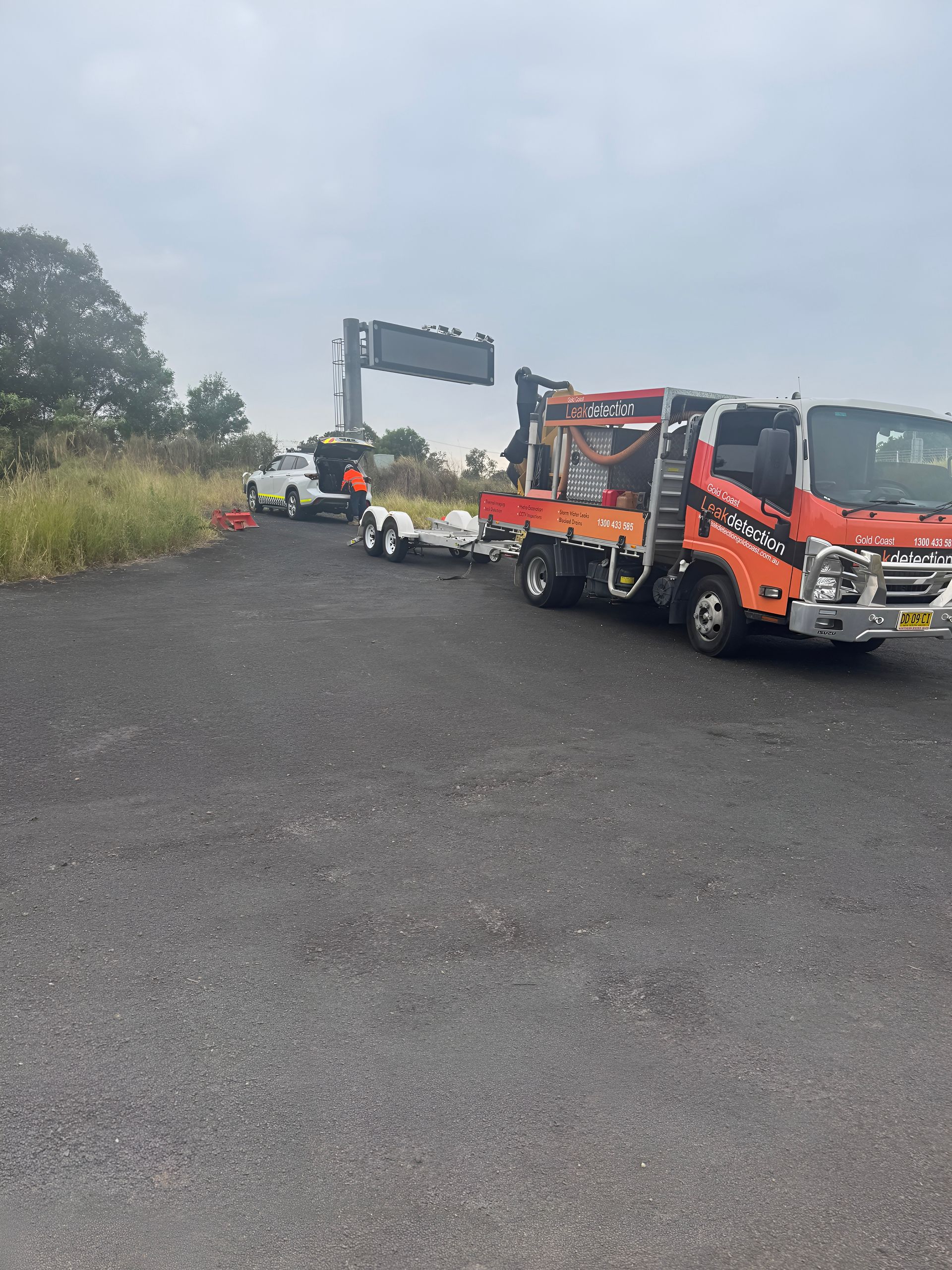 Orange Truck and Trailer With Road Sign and White Pickup — Gold Coast Leak Detection in Gaven, QLD