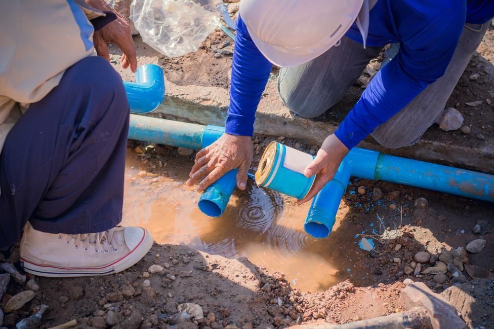 A Man is Kneeling Down Next to a Blue Pipe in the Dirt — Gold Coast Leak Detection in Mudgeeraba, QLD 