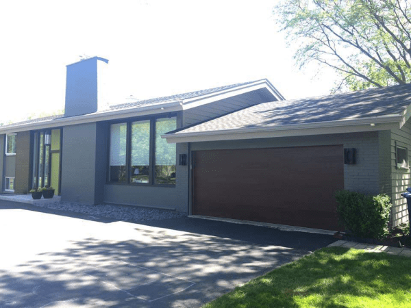 A gray house with a brown garage door and a chimney.