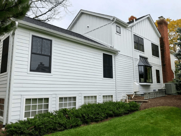 A large white house with black windows is sitting on top of a lush green lawn.