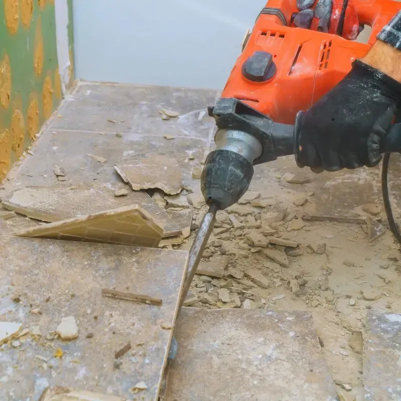 Man using drill to remove tile from floor.