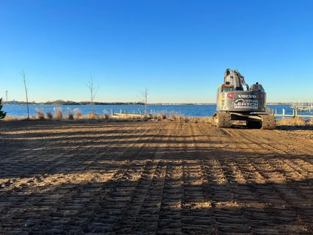 A bulldozer is driving down a dirt road next to a body of water.
