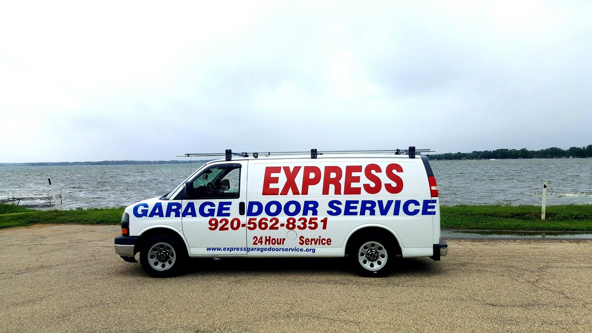 White garage service van with “Express Garage Door Service” parked by a waterfront road