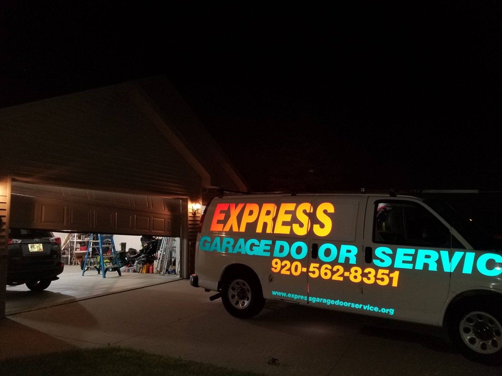 Tow truck with bright “Express Garage Door Service” sign at night outside a garage.